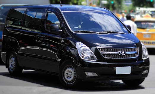 A nine-passenger rental car, a Hyundai Starex, is driving on the road