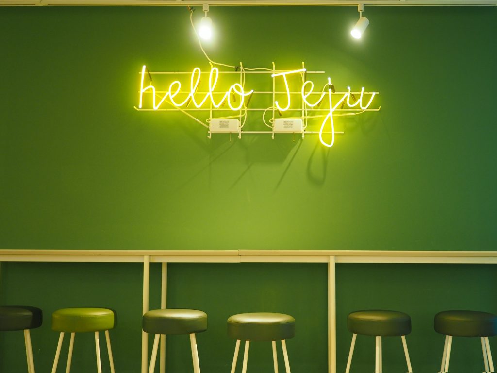 綠色的牆壁上，有著霓虹燈條寫著 hello jeju的字