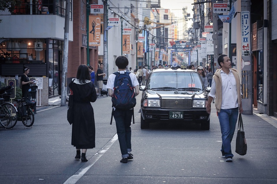大阪街道圖,一台計程車開在路面上,許多路人走在路上,車輛禮讓行人
