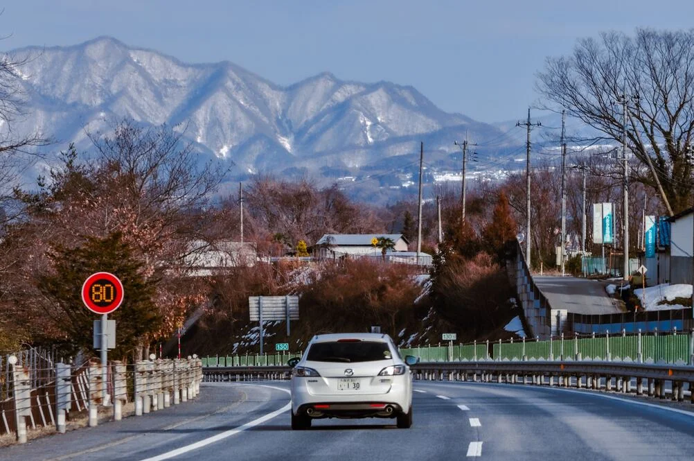 日本租車，租車上路畫面，高速公路景象，遠方有山脈，右側有民宅，速限八十公里