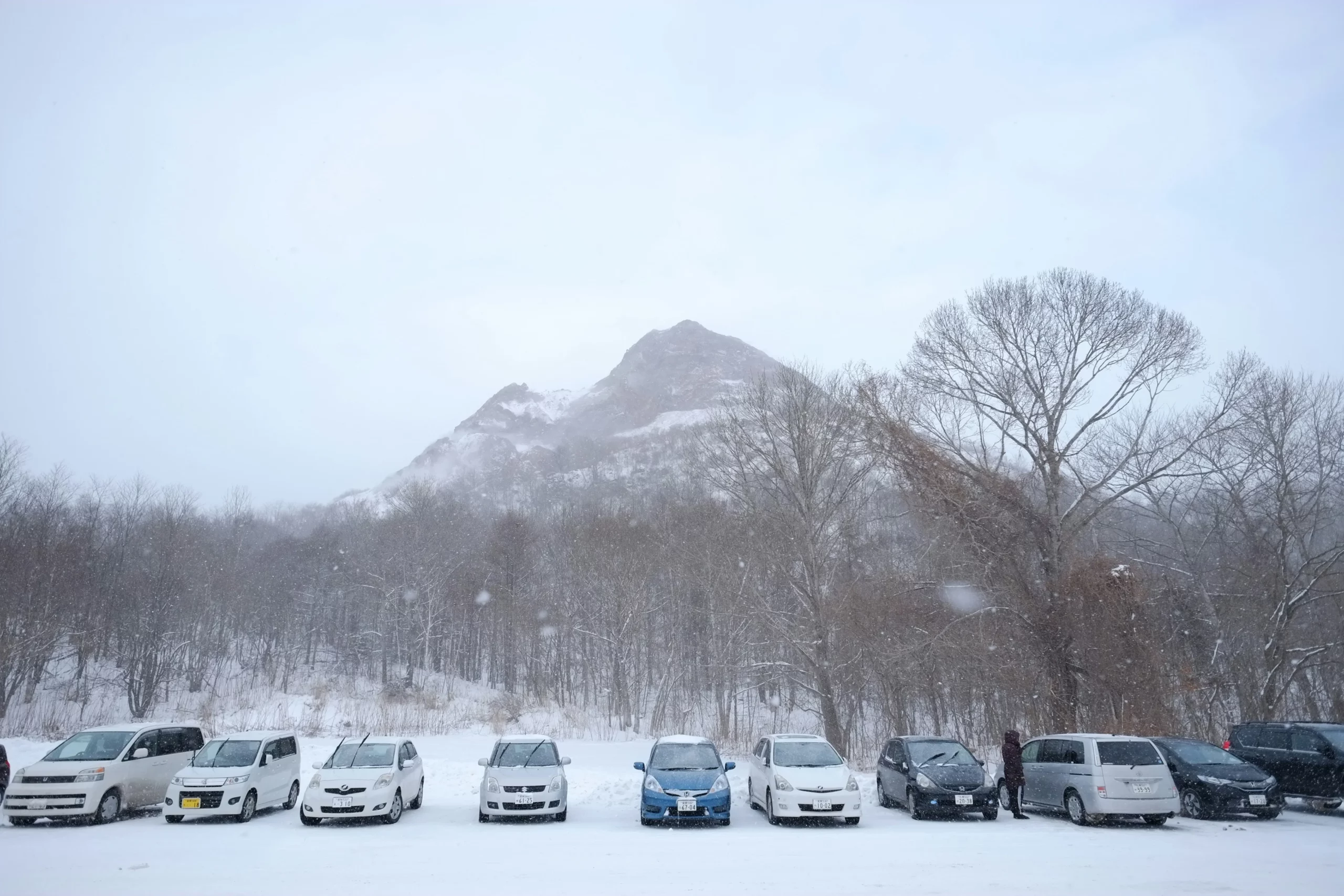 北海道租車,許多車輛在下雪的期間聽放在戶外,背景是一座山